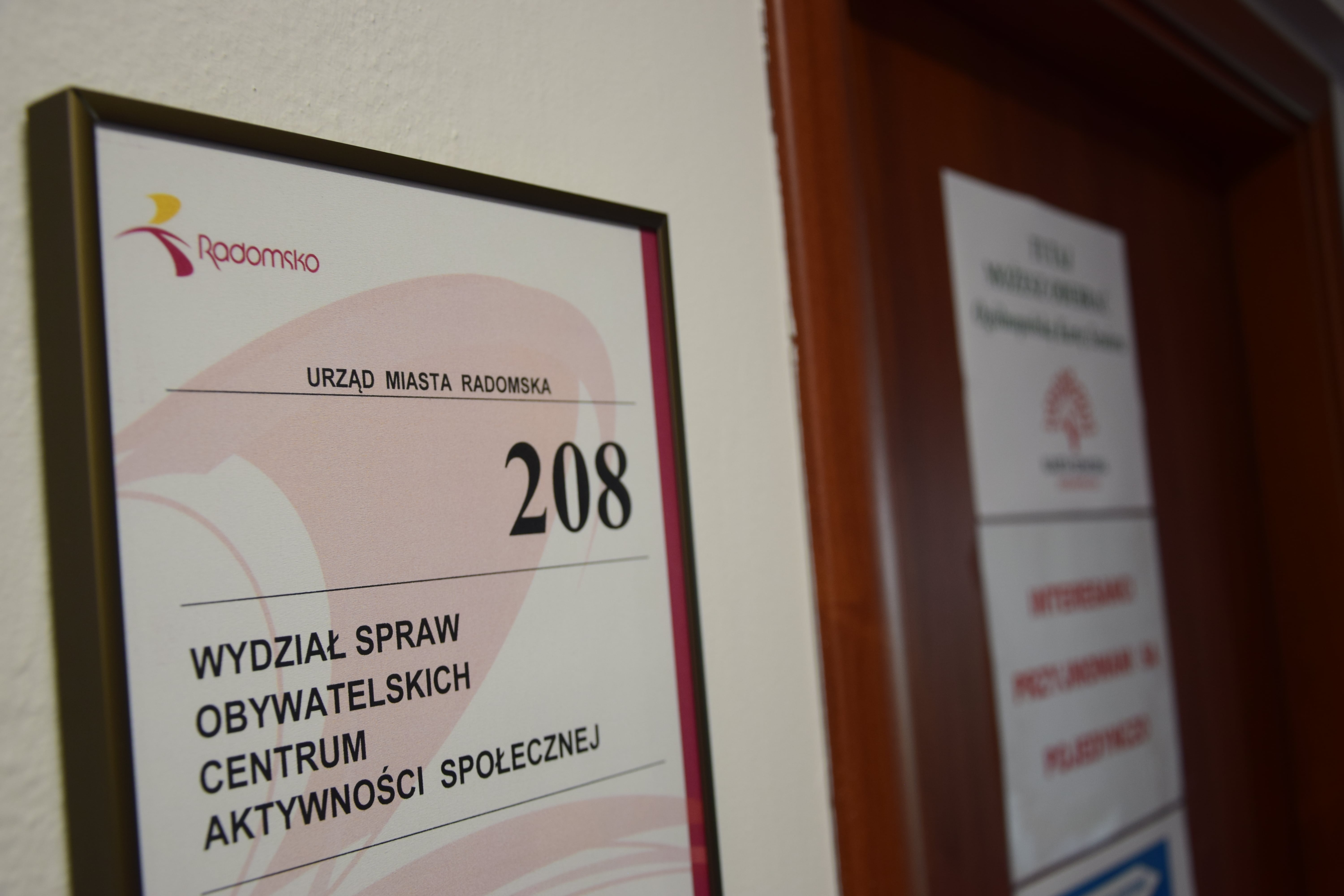zdjęcie przedstawia tabliczkę na drzwiach w budynku urzędu, pokój numer 208